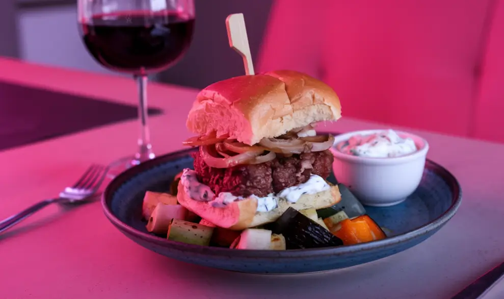 A gourmet burger with grilled onions and tzatziki sauce served on a bun, paired with roasted vegetables.