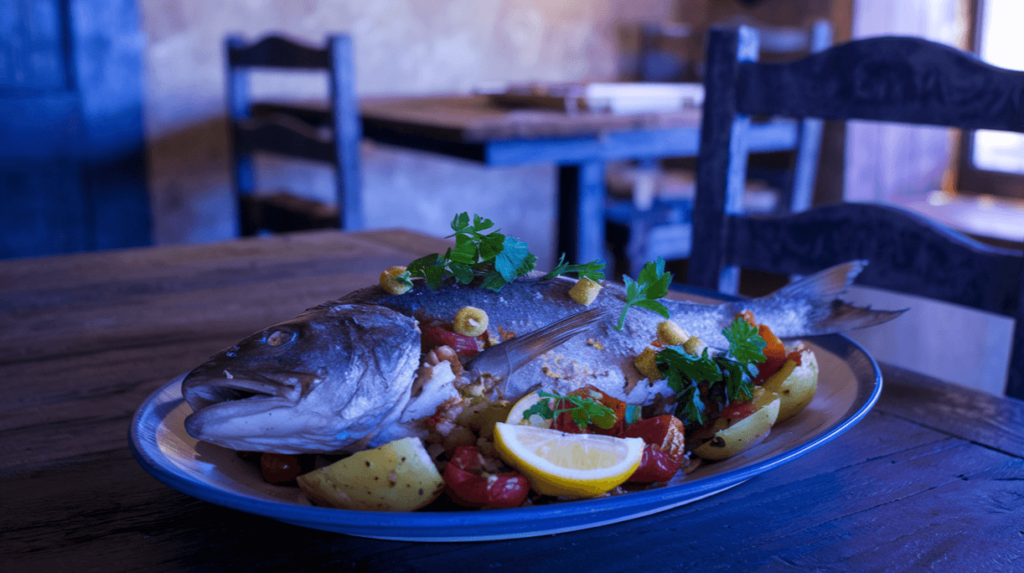 A presented whole Sea Bream served with roasted vegetables, potatoes, and fresh parsley on a rustic plate.