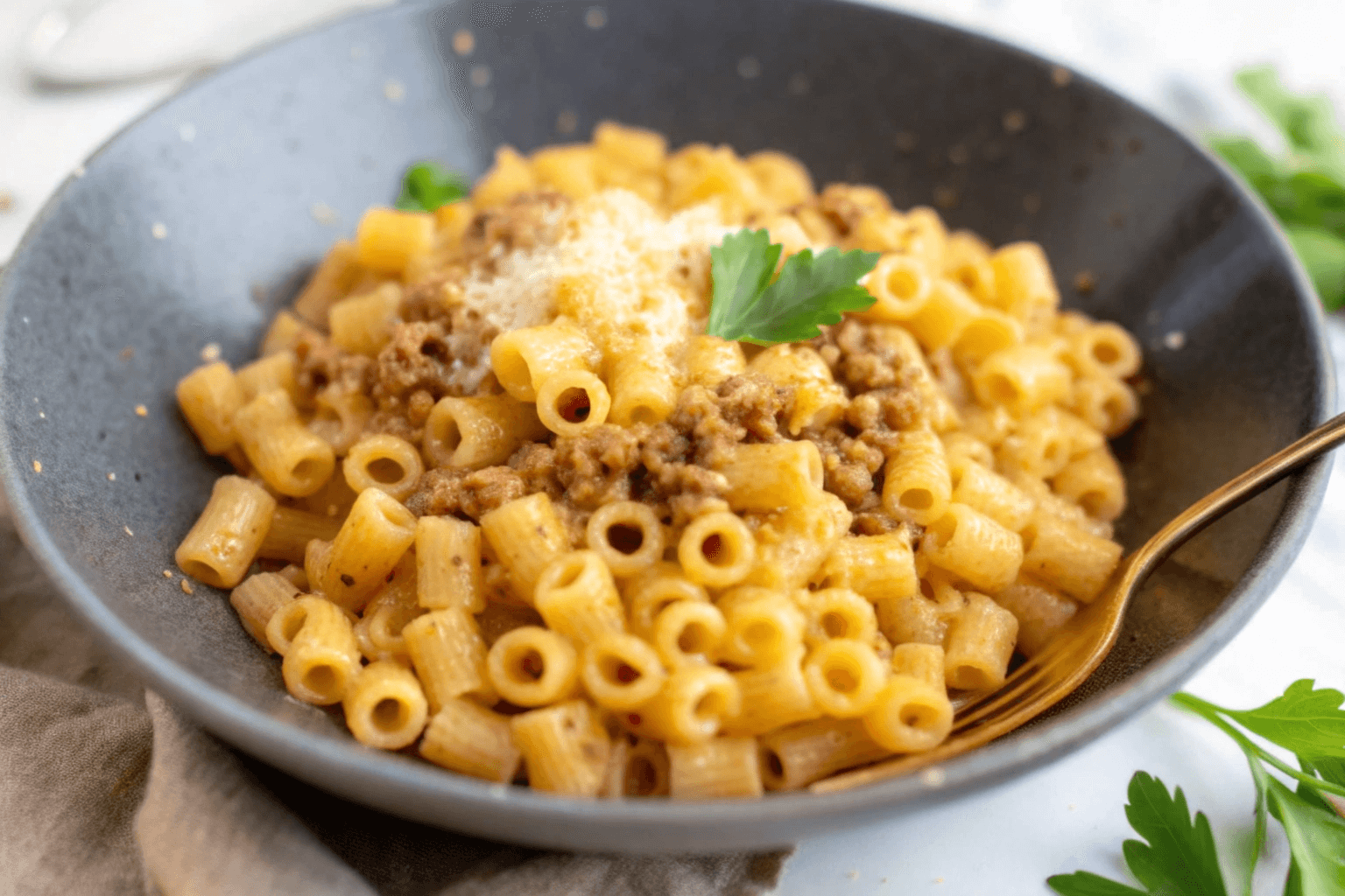 A bowl of creamy ditalini pasta mixed with ground meat, topped with grated cheese and garnished with a parsley leaf.