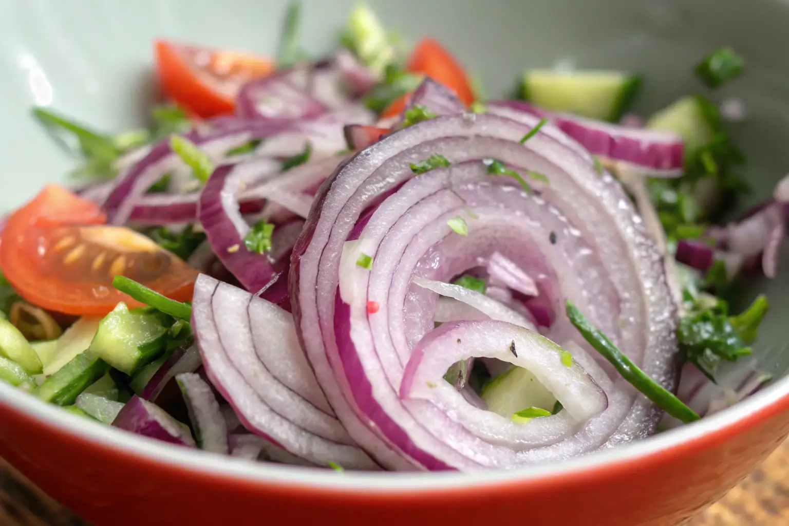 Red onion rings mixed with cherry tomatoes, cucumbers, and herbs in a vibrant salad bowl.