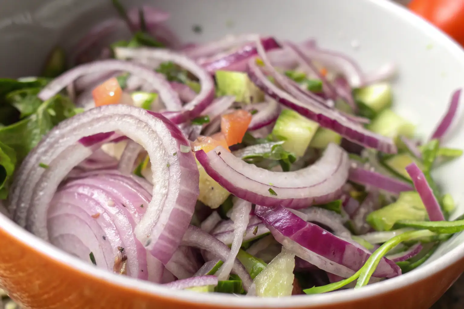 Thinly sliced purple onions, cucumbers, tomatoes, and fresh greens in a rustic salad bowl.