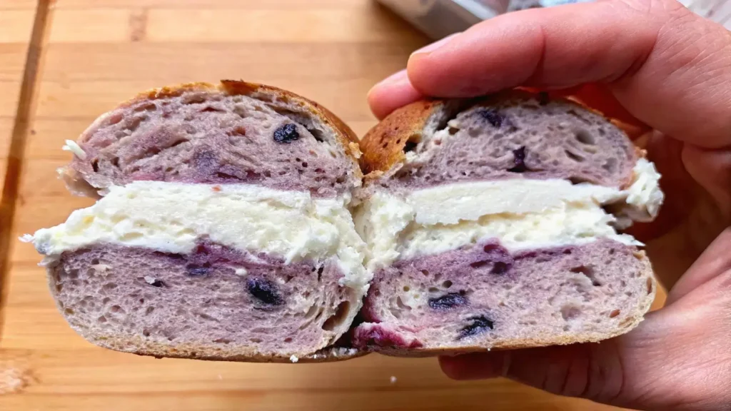 A sliced homemade blueberry bagel filled with creamy cheese.