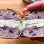 A sliced homemade blueberry bagel filled with creamy cheese.