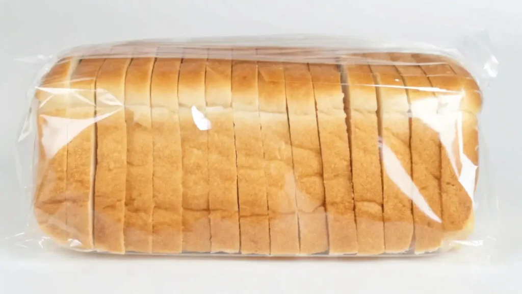  A loaf of pre-sliced, packaged white bread in clear plastic wrapping on a plain background.