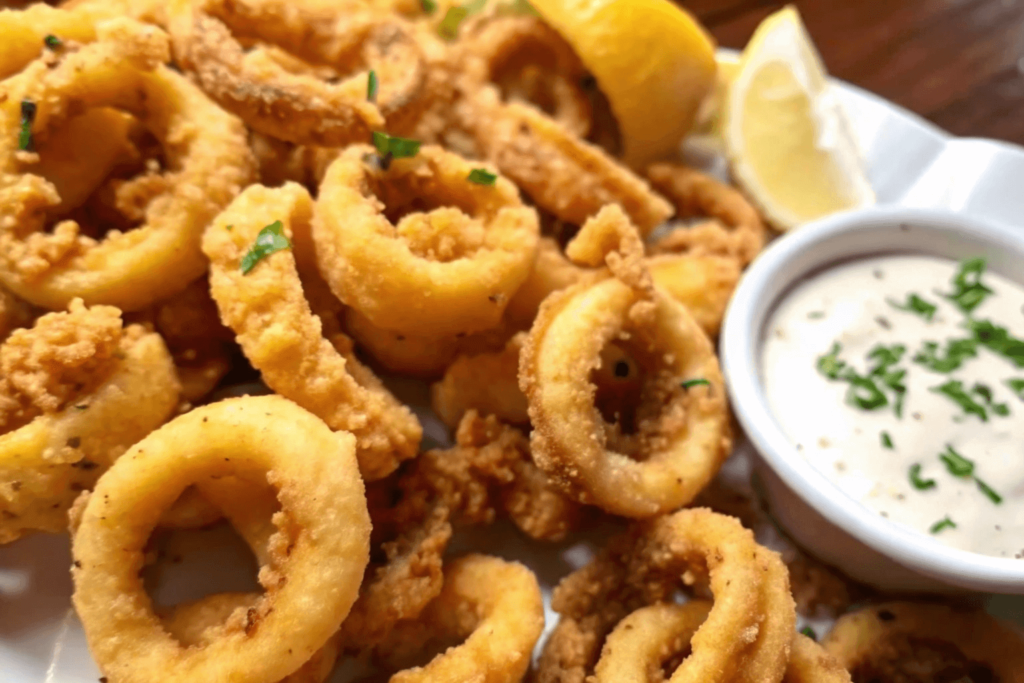 Golden fried calamari served with a creamy dipping sauce and lemon wedges for garnish.